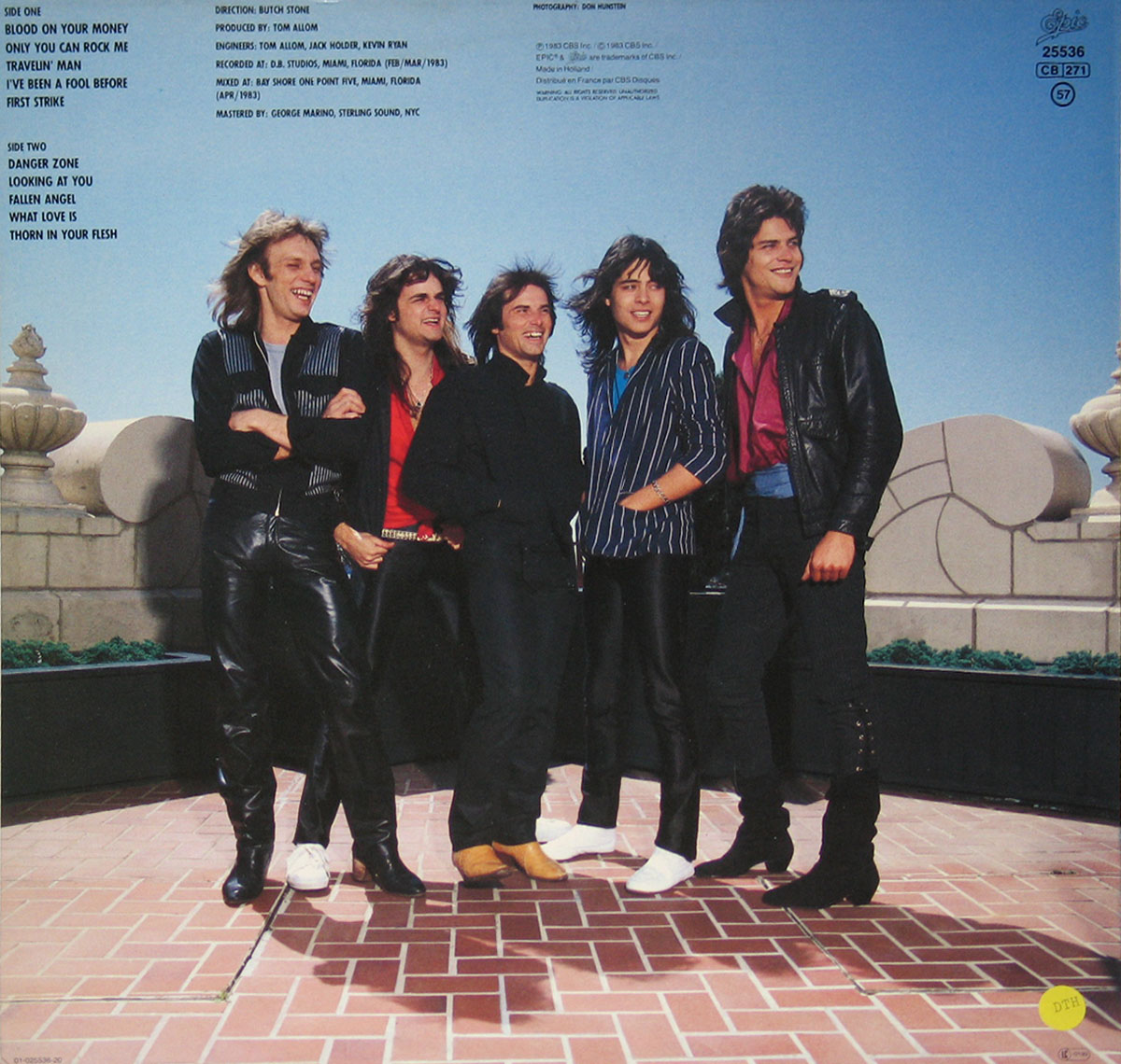 Back cover of Cobra's 1983 album First Strike featuring the band standing outdoors in front of a blue sky, with track listings and production credits on the upper left section of the image.
